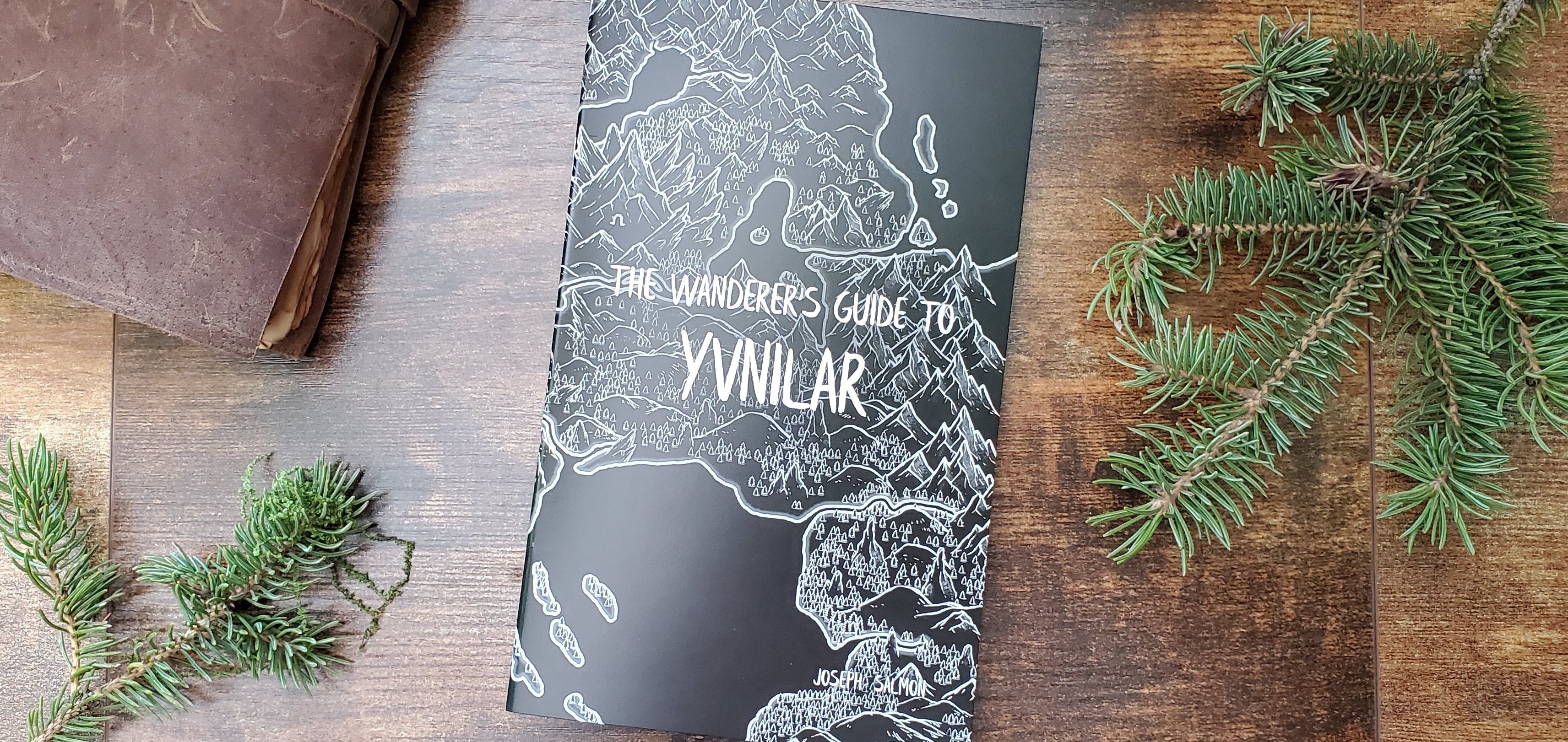 Book titled 'The Wanderer's Guide to Ynilar' on a wooden surface with greenery